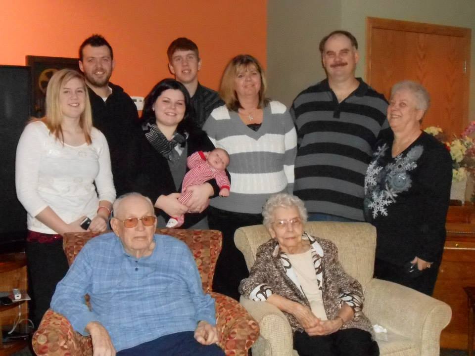 Elizabeth and Wilfred Schoen seated in armchairs, surrounded by Marilyn's family including a newborn baby